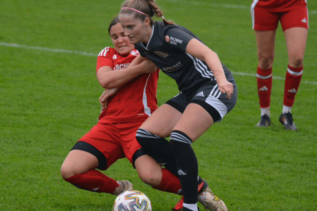Zwei Fußballspielerinnen kämpfen um den Ball auf dem Spielfeld während eines Spiels.