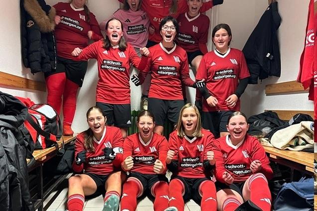 Gruppenszene von leidenschaftlichen Fu&szlig;ballspielerinnen in roten Trikots, die in einer Umkleidekabine feiern.