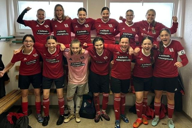 Gruppennfoto eines Fu&szlig;ballteams in roten Trikots, l&auml;chelnd und jubilierend in einer Umkleidekabine.