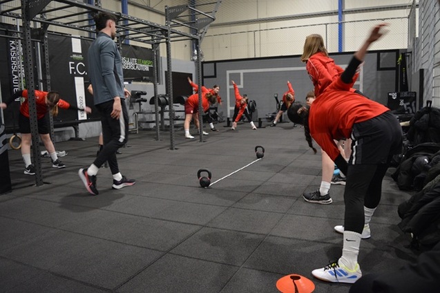 Gruppentraining im Fitnessstudio mit Sportlern in roten Outfits, die dehnen und sich vorbereiten.
