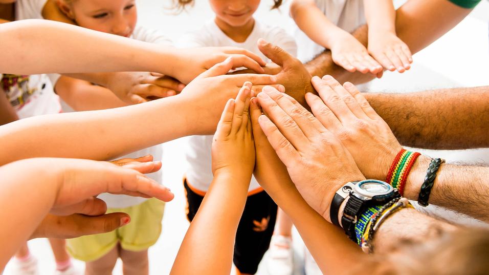 Kinder und Erwachsene legen ihre Hände in einem Kreis zusammen, symbolisieren Zusammenarbeit und Gemeinschaft.